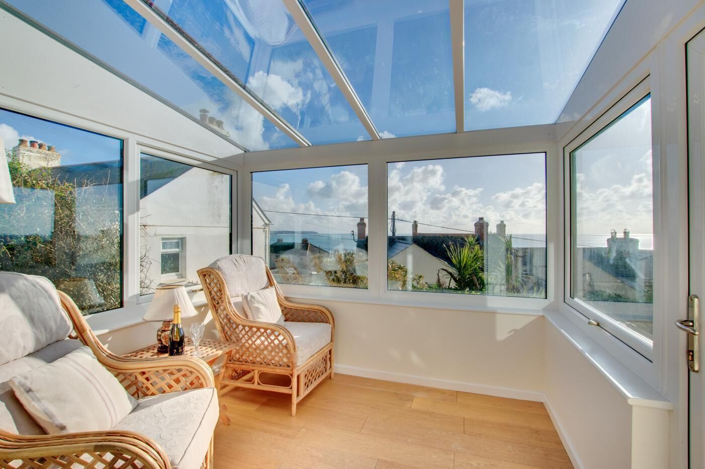 A sunlit room with a glass ceiling, wicker furniture, and a view of the sea.
