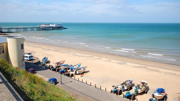 A beach with boats, a pier, and a building. - 4 Bed in Cromer (oc-1942) (Cromer)