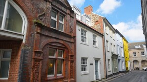 A street with a row of buildings, including a red brick building with arched windows and a white building with a door. - 4 Bed in Cromer (oc-1942) (Cromer)