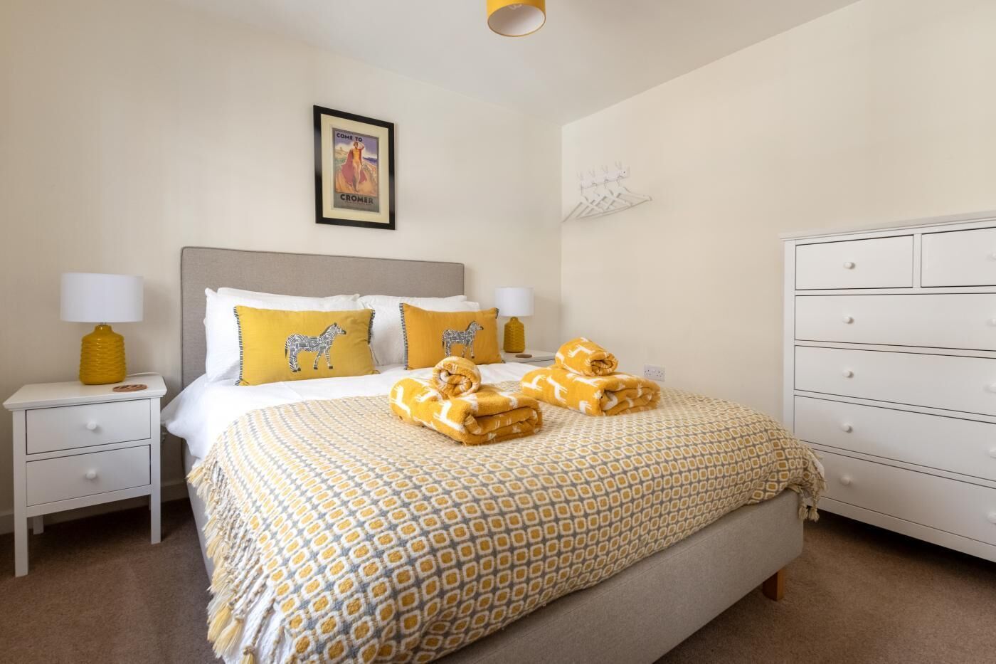 A neatly arranged hotel room with a large bed, two bedside tables with lamps, a dresser, and a framed picture on the wall.