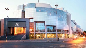 Een modern gebouw met een glazen gevel, een opvallende ingang en een trap naar de hoofdingang.