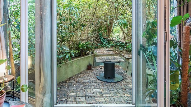 Ein Wintergarten mit Glastür und Zugang zu einem Gartenbereich mit Tisch und Stühlen.