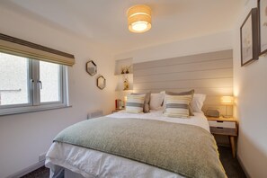 A bedroom with a bed, bedside lamps, a window, and a wall-mounted shelf with decorative items. - 1 Bed in Padstow (oc-p00735) (Padstow)