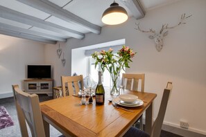 Et spiseområde med et træbord, stole, en vinflaske og en vase med blomster.