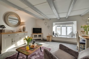 A living room with a TV, a round mirror, a dining table with a vase of flowers, and a window with a view. - 1 Bed in Padstow (oc-p00735) (Padstow)