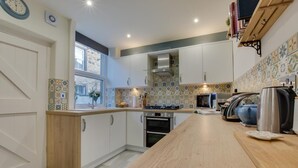Eine moderne Küche mit weißen Schränken, einer Holzausziehtheke, einem eingebauten Backofen, einer Mikrowelle und einem Wasserkocher.