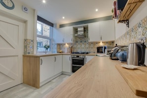 A modern kitchen with white cabinets, a wooden countertop, a built-in oven, a microwave, and a kettle.