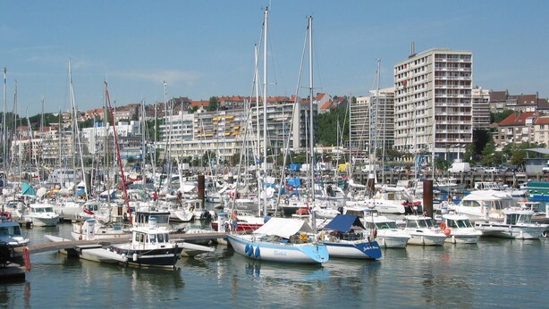 Un port de plaisance où de nombreux bateaux sont amarrés, entouré d’immeubles résidentiels et dominé par un imposant bâtiment à plusieurs étages.