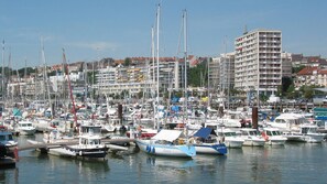 Uma marina com vários barcos atracados, cercada por edifícios residenciais e uma construção imponente de vários andares.