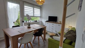 Une pièce avec un bureau en bois, deux chaises, un téléviseur posé sur un meuble et un canapé vert.