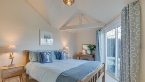 Een slaapkamer met een groot bed, nachtkastjes, een dressoir, een raam met gordijnen en een plafondlamp.