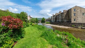 A riverside view with stone buildings, a grassy path, and lush greenery. - 2 Bed in Gayle (oc-ds912) (Hawes)