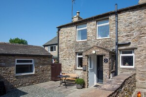 A stone house with a front door, a small porch, and a table with a bench.