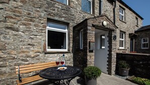A stone building with a bench and a table with drinks, a potted plant, and a sign indicating a pub. - 2 Bed in Gayle (oc-ds912) (Hawes)