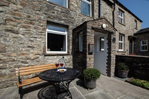 A stone building with a bench and a table with drinks, a potted plant, and a sign indicating a pub.