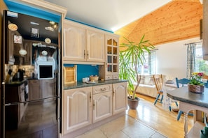 A modern kitchen with a built-in refrigerator, wooden cabinets, and a dining area with a table and chairs. - 2 Bed in Staithes (oc-wa071) (Staithes)