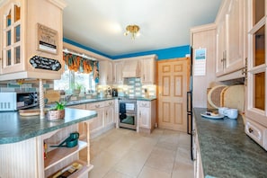 A kitchen with wooden cabinets, a microwave, a stove, and a refrigerator. - 2 Bed in Staithes (oc-wa071) (Staithes)