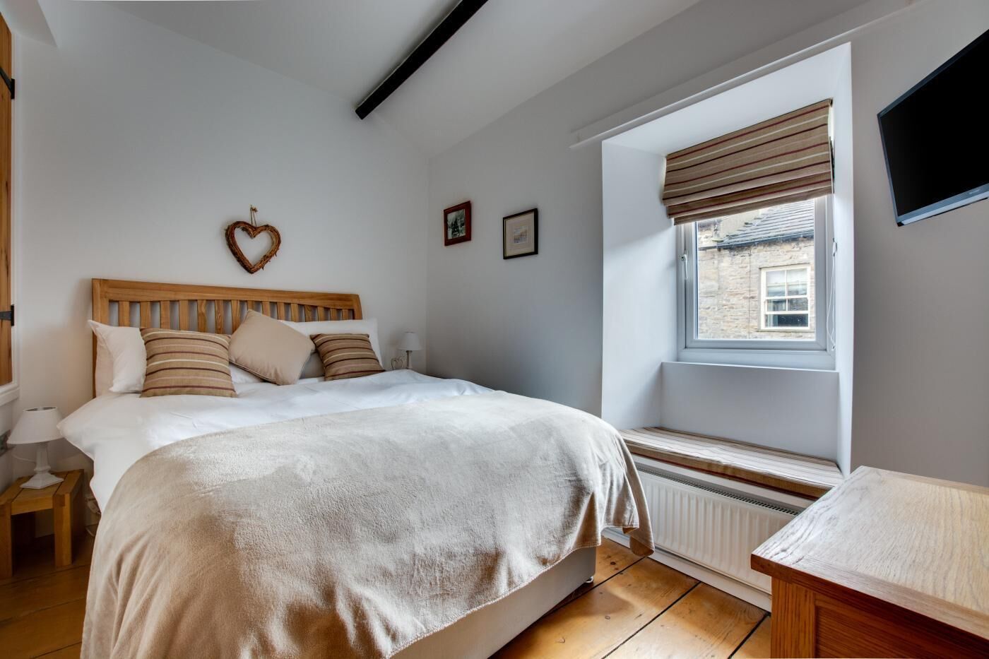 Ein Schlafzimmer mit einem hölzernen Bett, einem Fenster mit Aussicht, einem Heizkörper und einem an der Wand befestigten Fernseher.