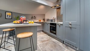 Uma cozinha moderna com armários cinza, uma ilha central com bancos e uma bicicleta como decoração de parede, além de um claraboia.