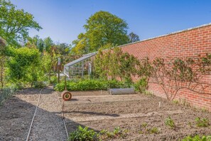 Un jardin avec un mur en briques, une structure métallique et diverses plantes.