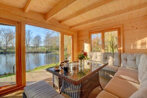 A wooden cabin with a glass table, sofa, and a view of a lake. - 3 Bed in Elsing (oc-1973) (Mill Street)