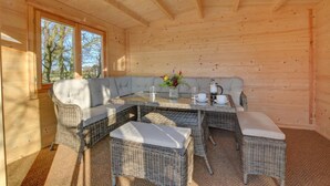 Un accogliente interno di una baita di legno con una grande panca imbottita, mobili in vimini e un tavolo apparecchiato per due.