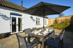 An outdoor dining area with a table set for four, surrounded by chairs, under a large umbrella. - 3 Bed in Elsing (oc-1973) (Mill Street)