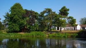 Un'ambientazione tranquilla lungo il fiume, con vegetazione rigogliosa e un piccolo ponte di legno.