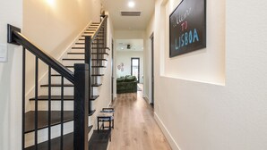 Un pasillo con una escalera, un letrero de bienvenida y un sofá al fondo.