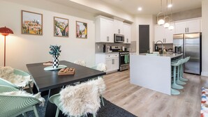 Una cocina moderna con armarios blancos, una isla central con taburetes de bar, una mesa de comedor con sillas y obras de arte en las paredes.