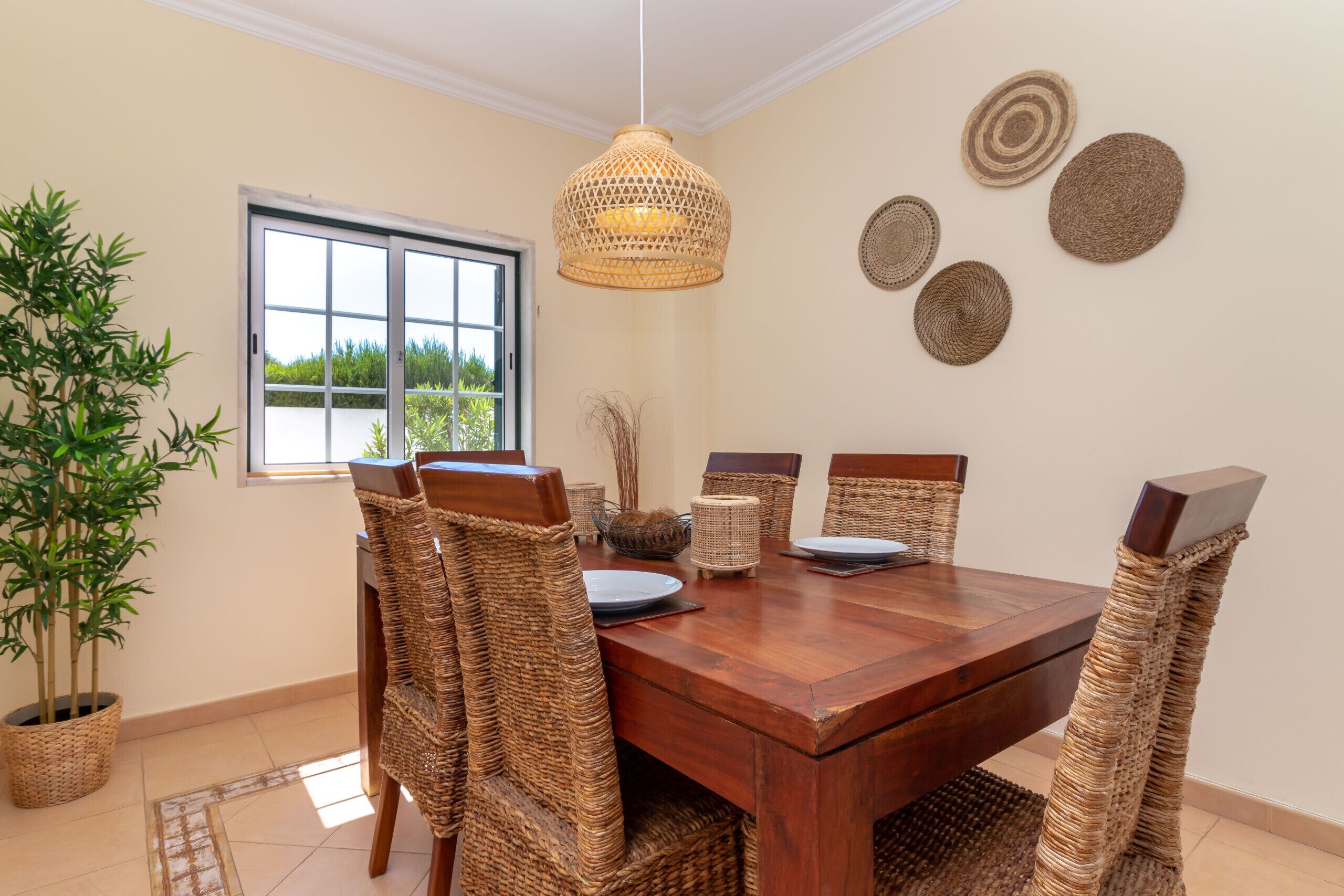 A dining area with a wooden table, wicker chairs, and a hanging light fixture.