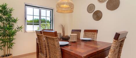 A dining area with a wooden table, wicker chairs, and a hanging light fixture.