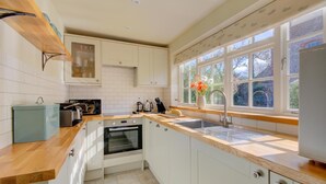 Een keuken met witte kasten, een houten aanrecht, een ingebouwde oven en een raam met uitzicht op bomen.