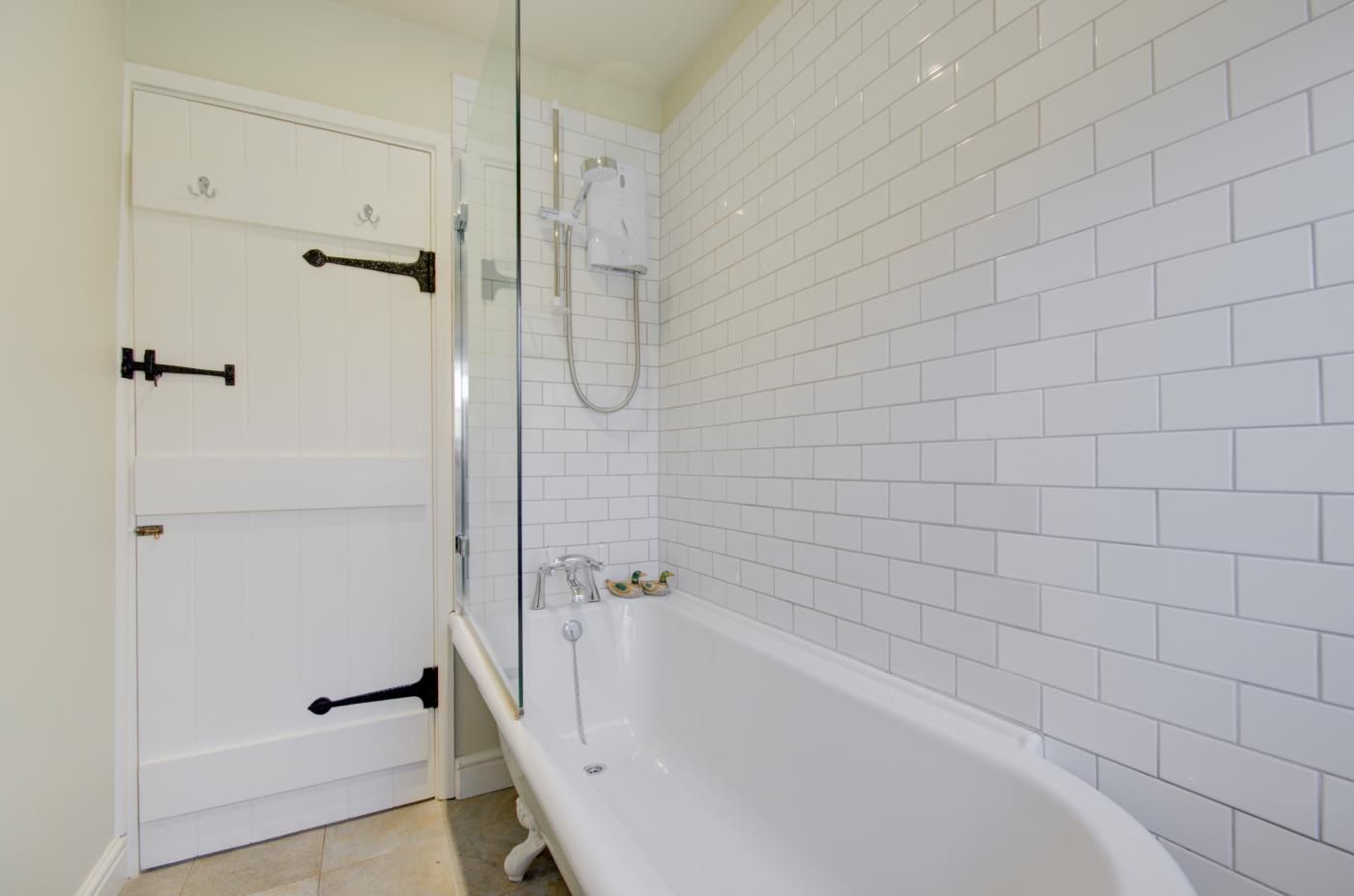 A bathroom with white tiled walls, a white bathtub, and a glass-enclosed shower area.