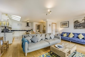 Ein modernes Wohnzimmer mit einem grauen Sofa, einem blauen Sofa, einem Holztisch und einer Küche im Hintergrund.