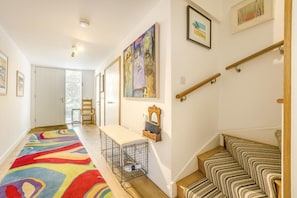 Ein Flur mit farbenfrohem Teppich, einer Bank, einem kleinen Tisch mit Spiegel und einer Treppe mit gestreiften Kissen.