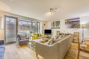A modern living room with a sofa, armchairs, a coffee table, a TV, and a dining area with chairs and a table. - 4 Bed in Southwold (oc-hswall) (Southwold)