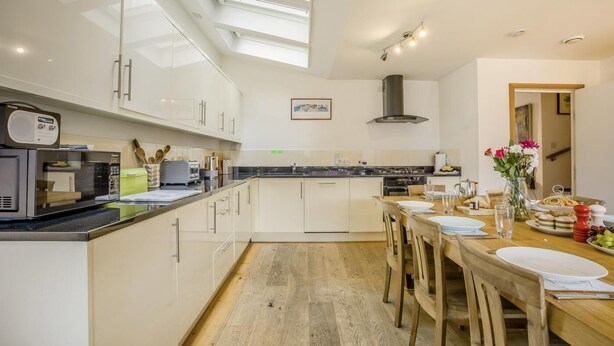 A modern kitchen with a skylight, a dining area with a wooden table, and a view of the hallway. - 4 Bed in Southwold (oc-hswall) (Southwold)