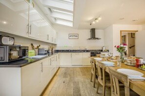 A modern kitchen with a skylight, a dining area with a wooden table, and a view of the hallway. - 4 Bed in Southwold (oc-hswall) (Southwold)