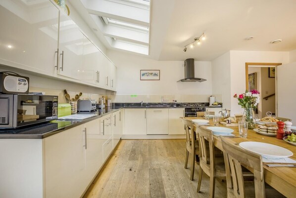A modern kitchen with a skylight, a dining area with a wooden table, and a view of the hallway.