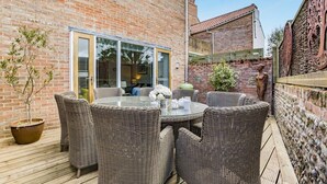 A patio with wicker furniture, a glass table, and a brick wall. - 4 Bed in Southwold (oc-hswall) (Southwold)