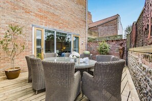 A patio with wicker furniture, a glass table, and a brick wall.