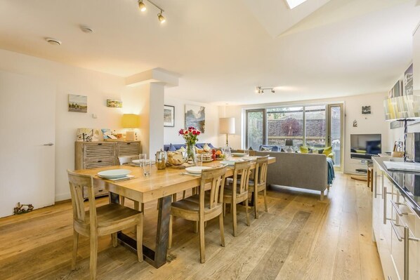 A modern kitchen with wooden cabinetry, a dining table set for four, and a large window providing a view of the outdoors.