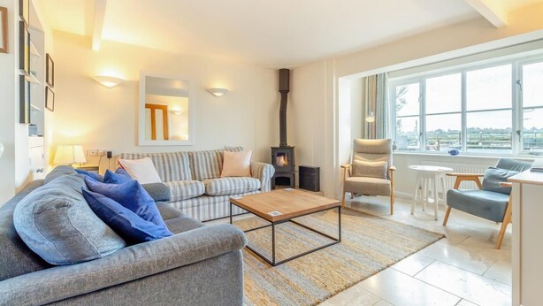A modern living room with a sofa, armchair, and a fireplace. - 3 Bed in Southwold (oc-hshore) (Southwold)