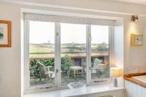 A room with a large window, a table with chairs, a lamp, and a clock on the wall. - 3 Bed in Southwold (oc-hshore) (Southwold)