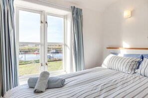 A hotel room with a bed, curtains, a view of boats on water, and a headboard. - 3 Bed in Southwold (oc-hshore) (Southwold)
