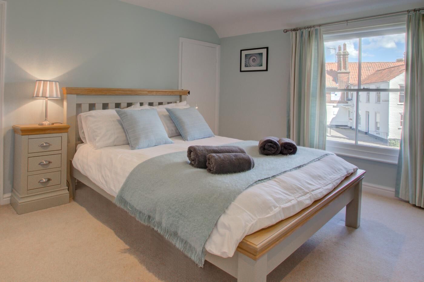 A bedroom with a bed, bedside table, lamp, and a window with a view.