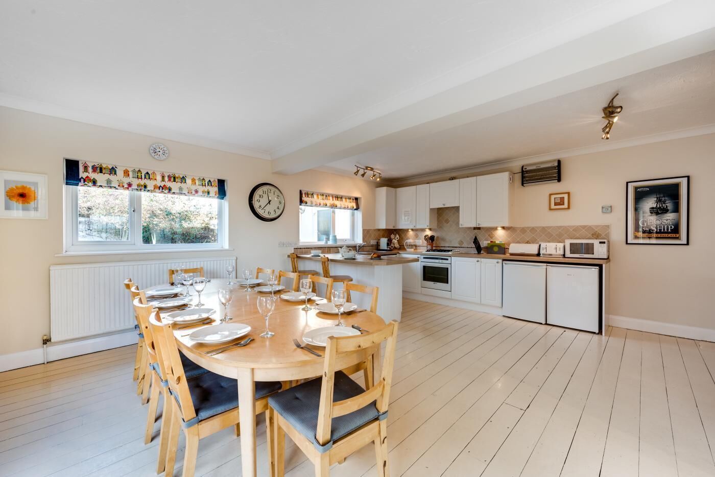 A spacious kitchen with white cabinets, a dining area with a wooden table and chairs, and a large window with a view of greenery.