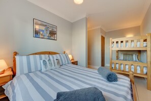 A bedroom with a bed, a wooden bunk bed, a nightstand, a lamp, and a framed picture on the wall. - 4 Bed in Southwold (oc-hhigh) (Southwold)