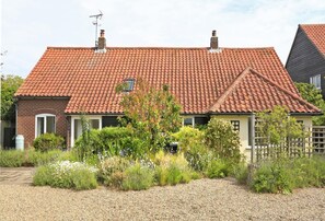 Ein zweistöckiges Haus mit rotem Ziegeldach, Backsteinwänden und einem Garten mit verschiedenen Pflanzen und Blumen.